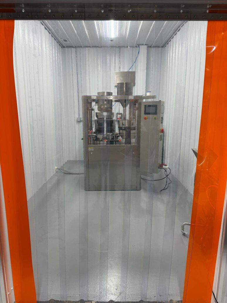 Looking into the encapsulation room through its strip curtain, the machine standing alone on the floor